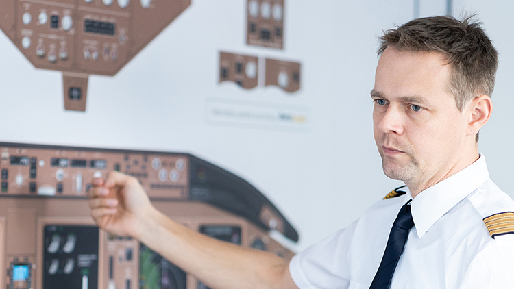 Ein Pilot steht vor einer Schautafel, die ein Flugzeugcockpit zeigt